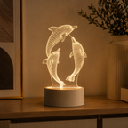 A 3D LED light lamp featuring three dolphins in a warm glowing wireframe design, set on a wooden table in a cozy room next to a framed picture and a vase.