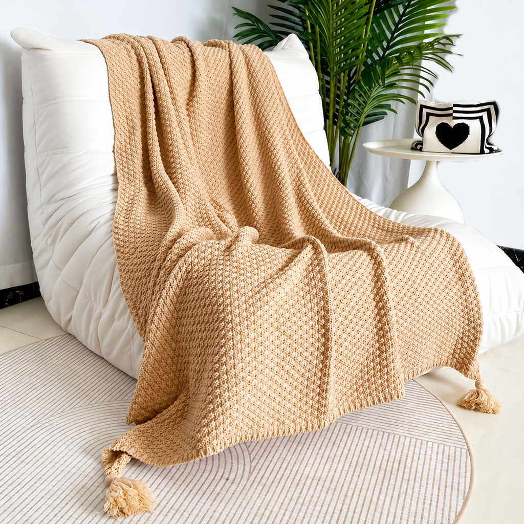 Khaki acrylic knit throw blanket with pebbled stripes and corner tassels on a cream chair