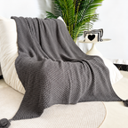 Gray acrylic knit throw blanket draped over a cream chair beside a plant