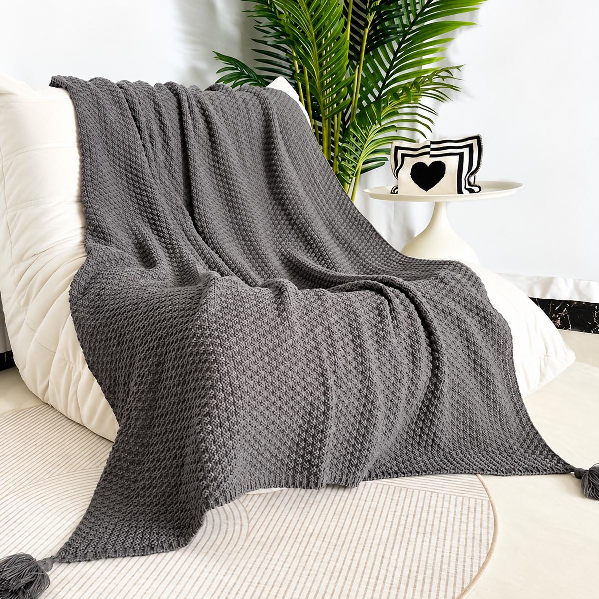 Gray acrylic knit throw blanket draped over a cream chair beside a plant