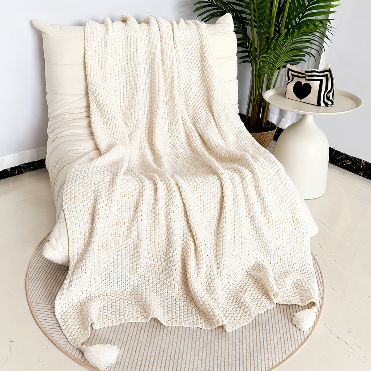 Beige acrylic knit throw blanket spread over a cream chair with corner tassels visible