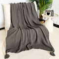 Gray acrylic knit throw blanket spread over a cream chair with corner tassels visible
