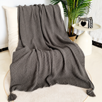 Gray acrylic knit throw blanket spread over a cream chair with corner tassels visible