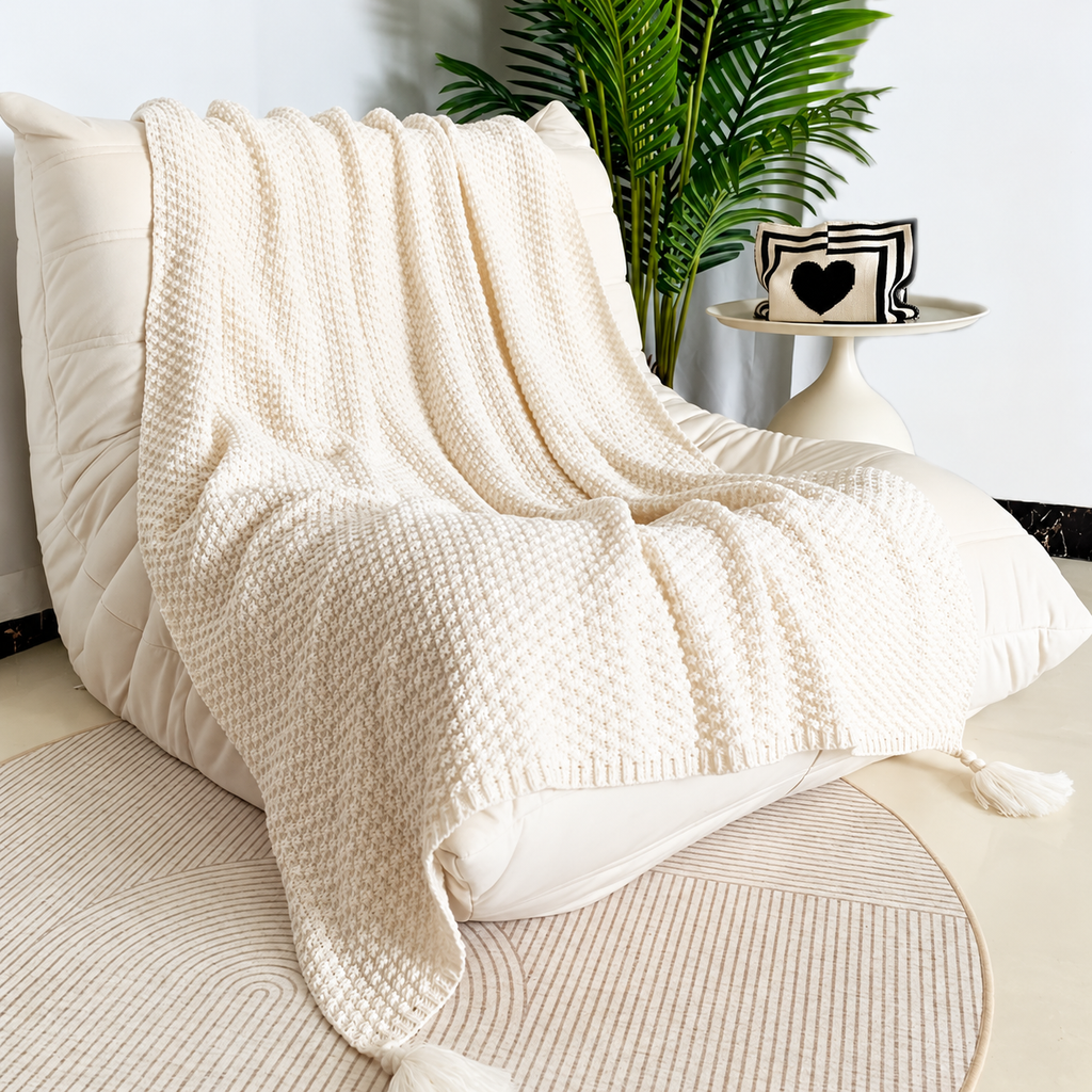 Beige acrylic knit throw blanket draped over the back and seat of a cream chair