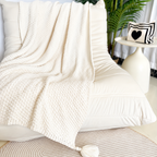 Beige acrylic knit throw blanket spread diagonally over a cream chair