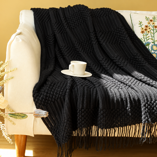 Black textured acrylic knit throw blanket with fringe draped over a cream chair