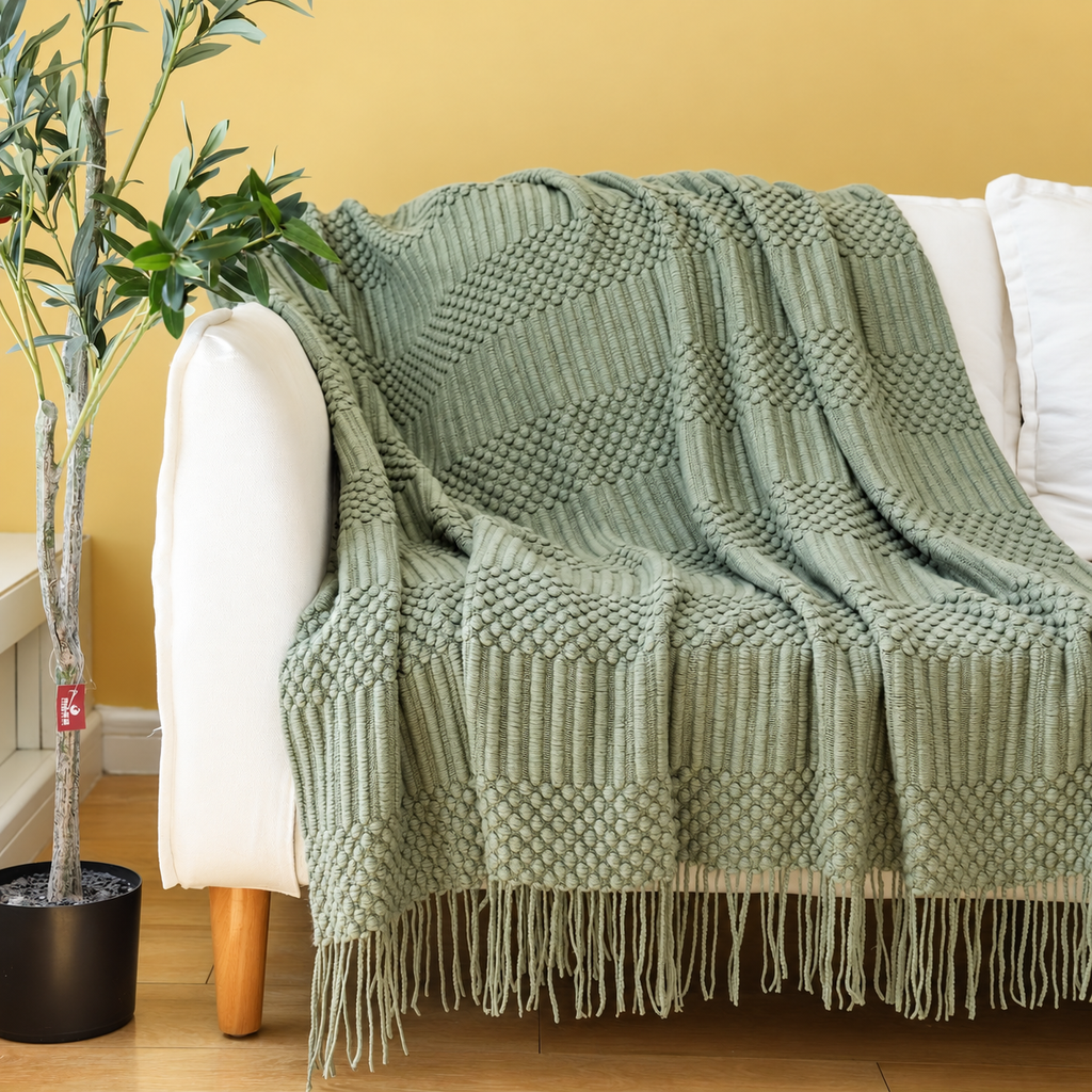 Sage green textured acrylic knit throw blanket draped over a cream chair