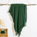 Green textured acrylic knit throw blanket hanging over a branch