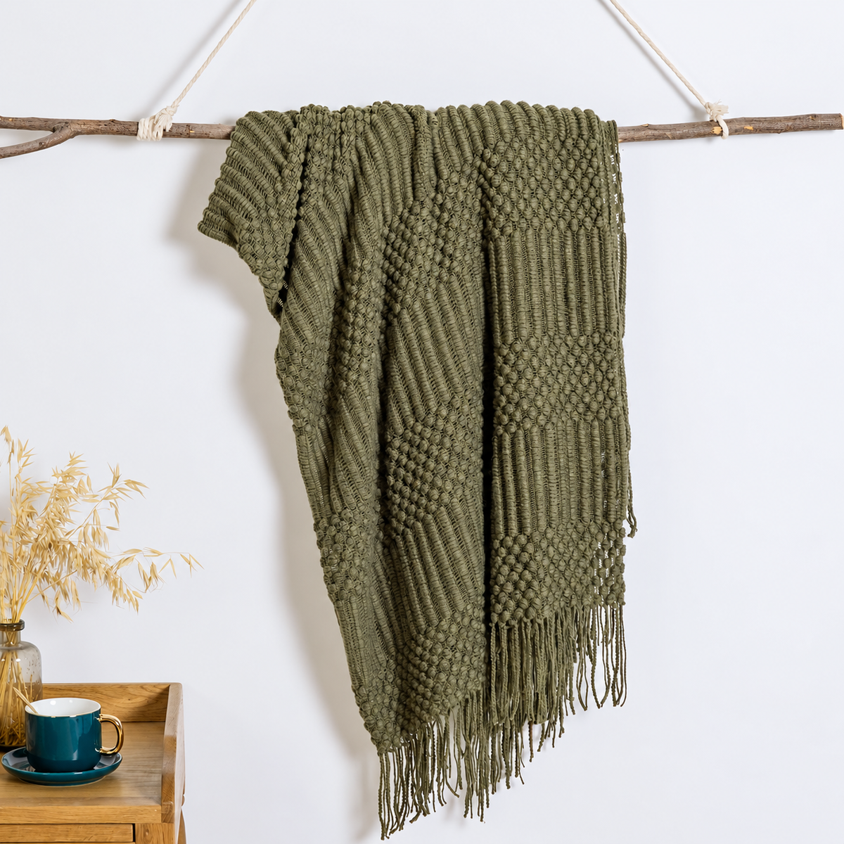 Olive textured acrylic knit throw blanket hanging over a branch