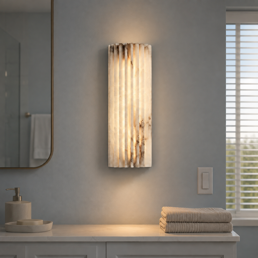 Vertical wall sconce glowing above a bathroom counter with folded towels.