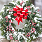 Snowy artificial cedar and red berry sprigs arranged in a wreath with a separate red bow