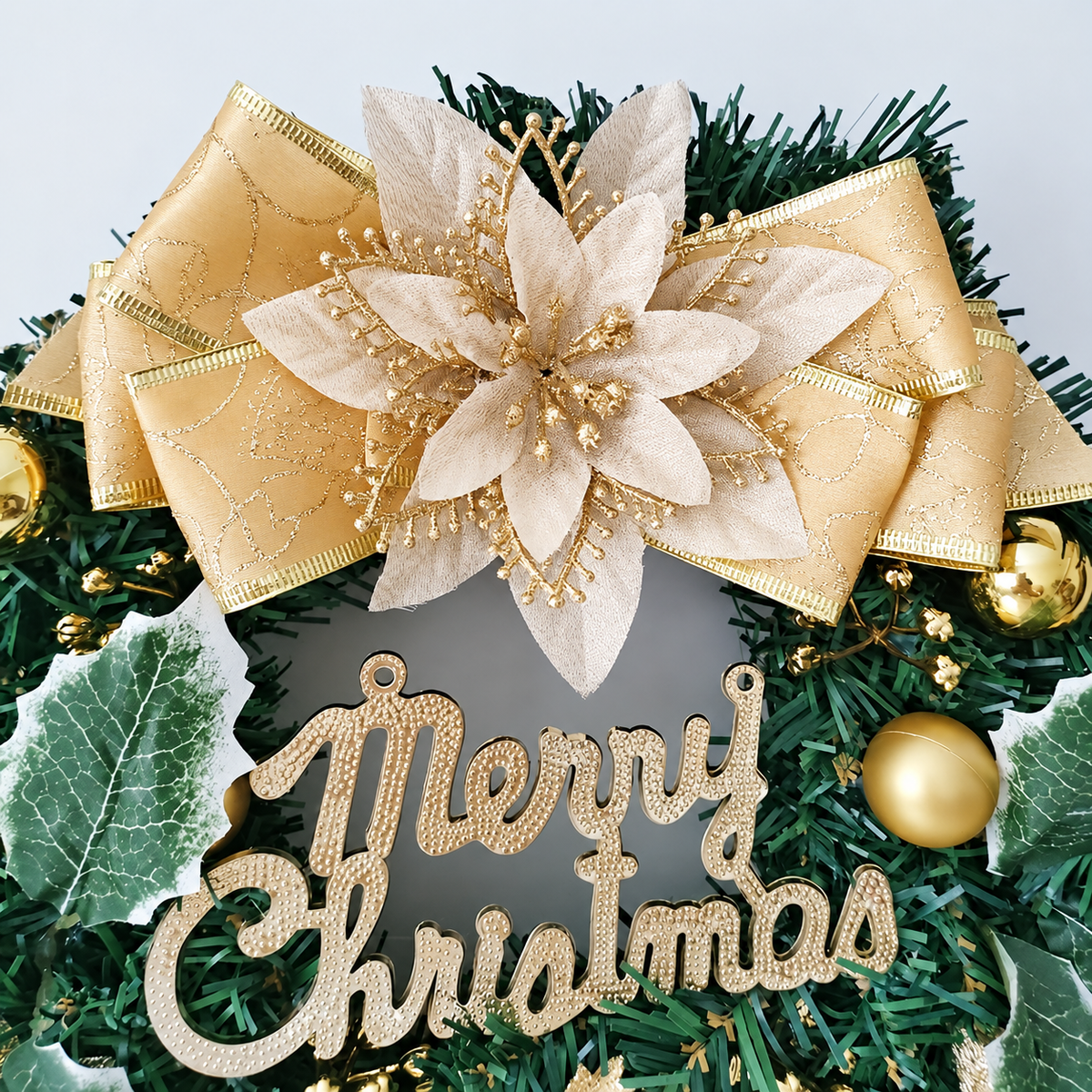 Close up of gold bow flower Merry Christmas lettering and bells on an artificial wreath