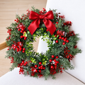 Artificial Christmas wreath with red berries green foliage and red bow against a pale wall