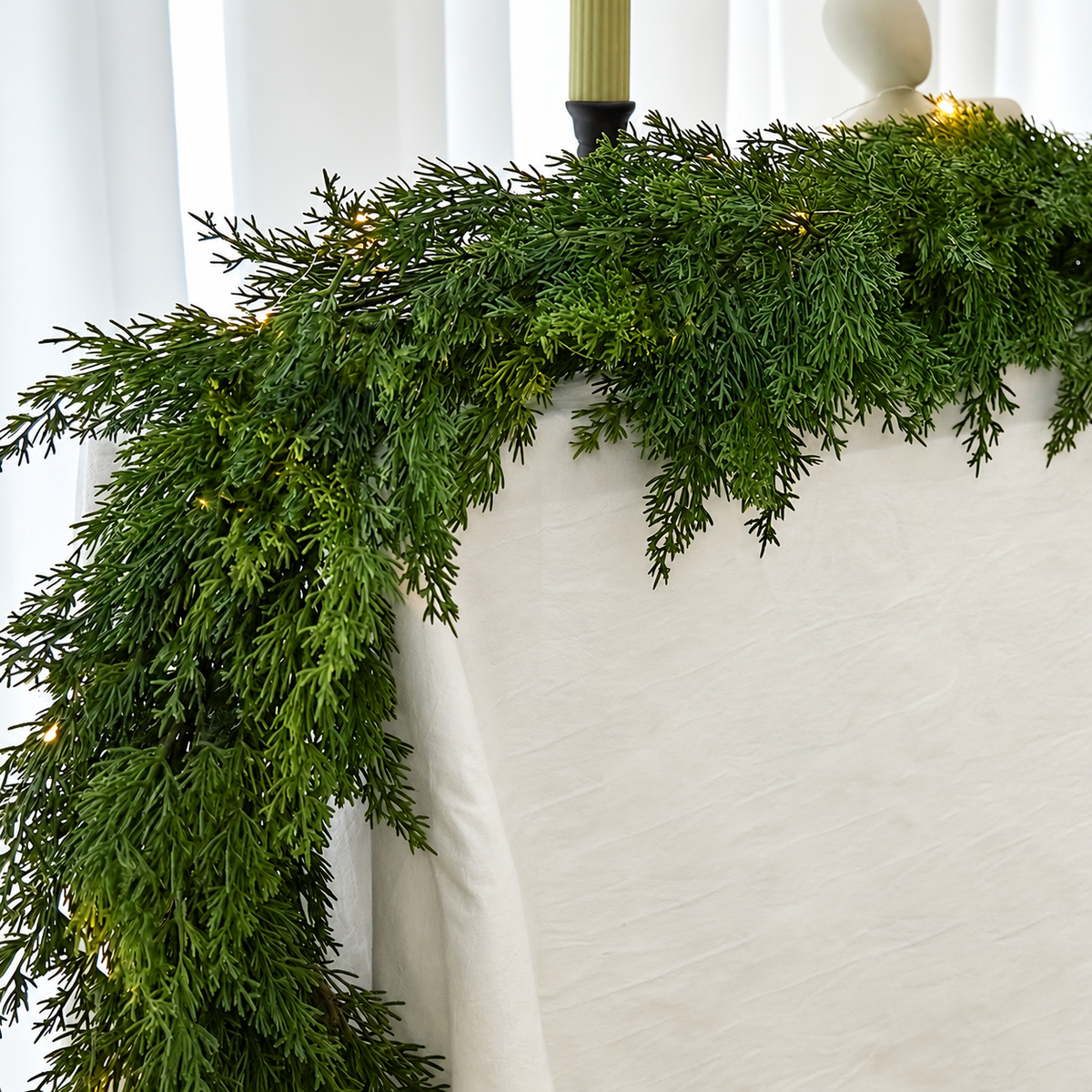 Artificial green cypress garland draped over a white mantel beside a window
