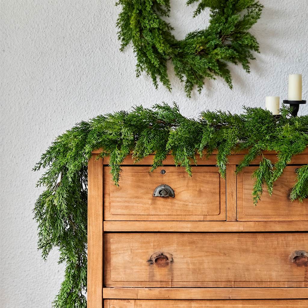 Artificial cypress garland displayed on a wooden dresser below a wreath