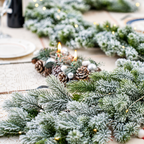 Close up of snow flocked garland on a dining table beside a separate candle arrangement