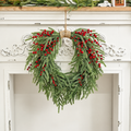 Artificial pine and red berry wreath hanging from a fireplace mantel