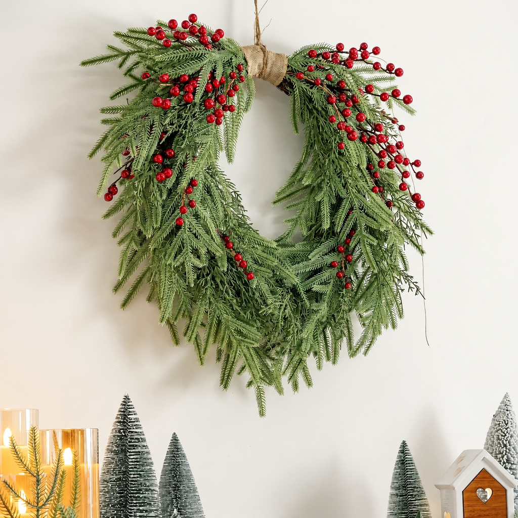 Draped artificial pine and berry wreath hanging above candles and small decorative trees