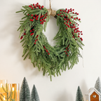Draped artificial pine and berry wreath hanging above candles and small decorative trees
