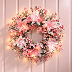Artificial pink floral wreath on a pink wall shown with separate string light styling