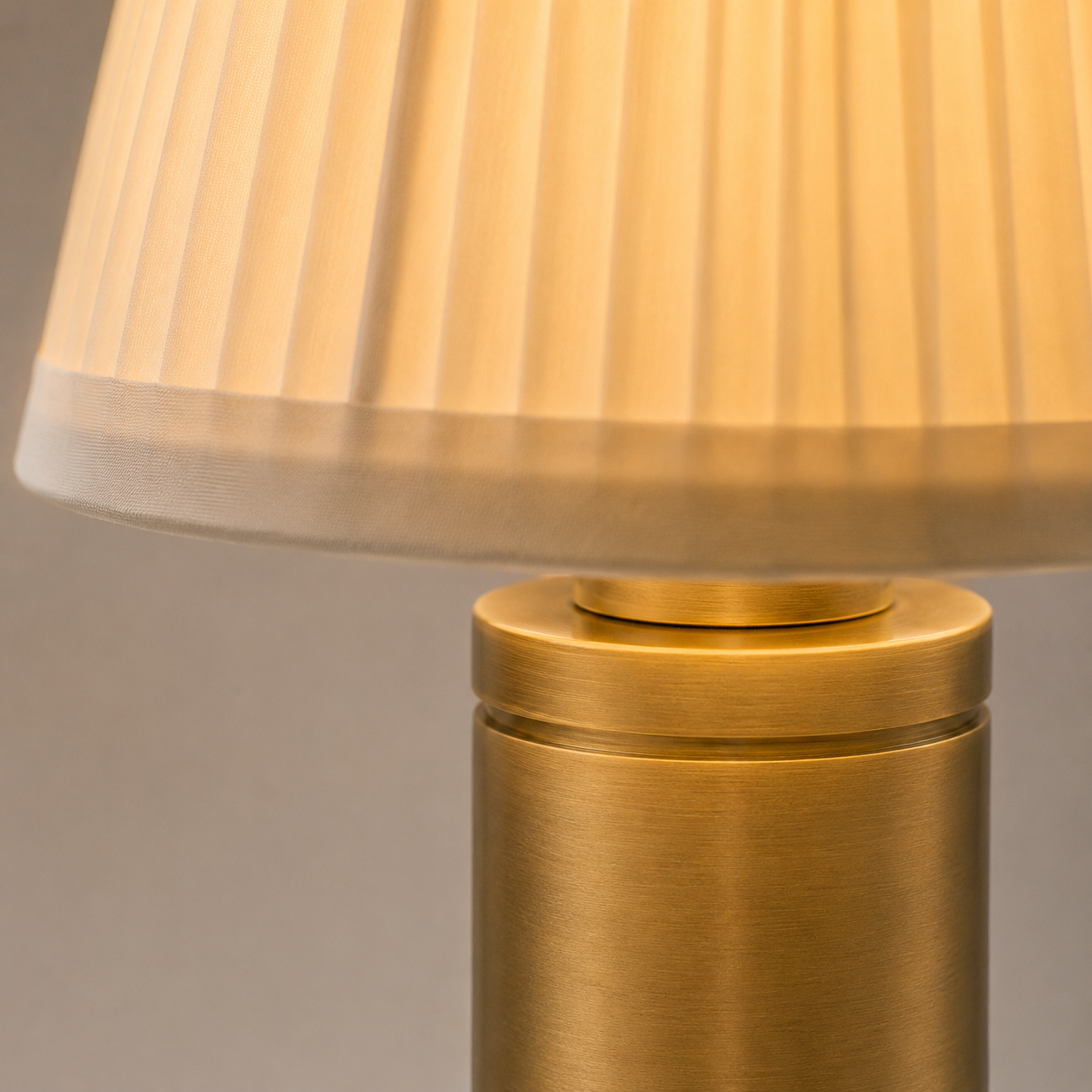 Table lamp close-up showing the pleated cream shade, gold neck, and upper section of the metal stem.