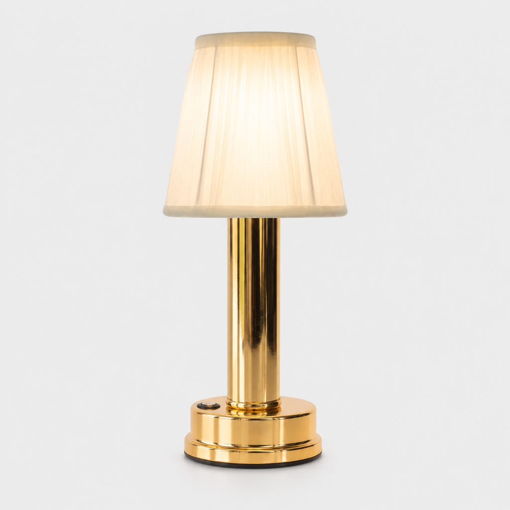Gold table lamp with a pleated cream shade glowing against a plain light-gray studio background.