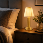 Gold table lamp glowing on a bedside table beside a made bed in a warm, softly lit bedroom.