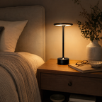 Black table lamp glowing on a bedside table beside a bed in a warmly lit room.