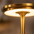 Close-up of the table lamp’s round gold shade, illuminated diffuser, and flared stem.