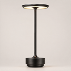 Black table lamp with a round shade, slim stem, circular base, and warm light on a plain background.