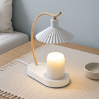 White candle warmer lamp with a curved wood arm warming a plain jar candle on a light oak table.