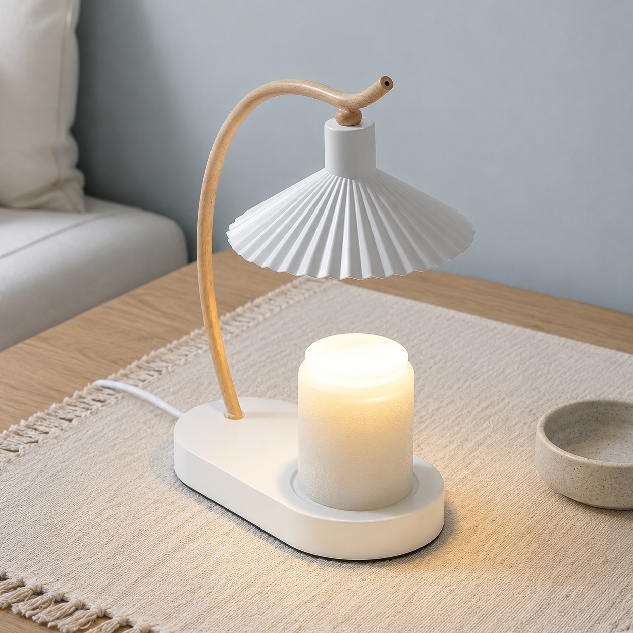 White candle warmer lamp with a curved wood arm warming a plain jar candle on a light oak table.