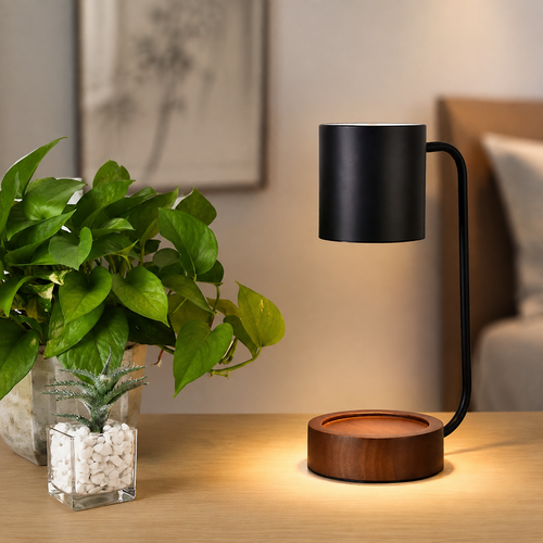 Black candle warmer lamp with wood base beside a plant.