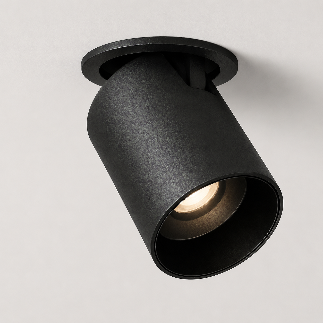 Black adjustable cylindrical LED ceiling spotlight glowing warm white against a neutral ceiling.
