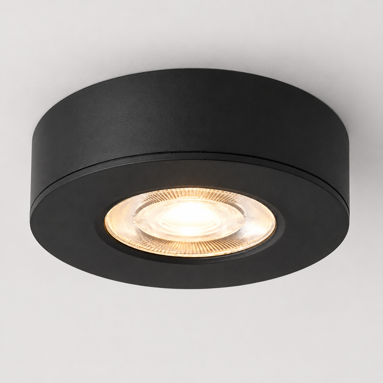 Black ultra-thin round LED ceiling spotlight glowing warm white on a white ceiling.