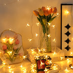 Cherry blossom fairy lights arranged around a vase of flowers.