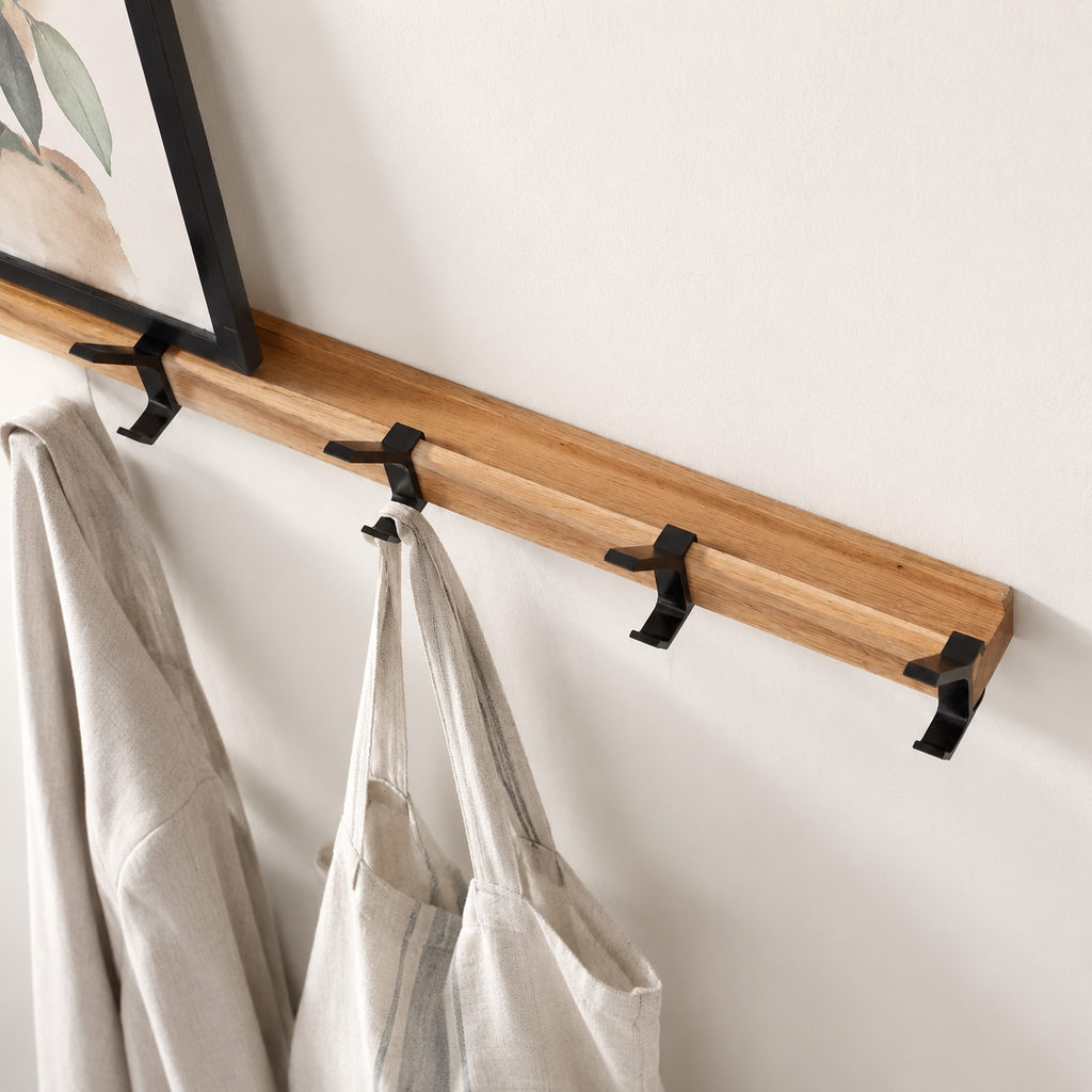 Black double-hook coat rack with wood rail holding light linen garments.
