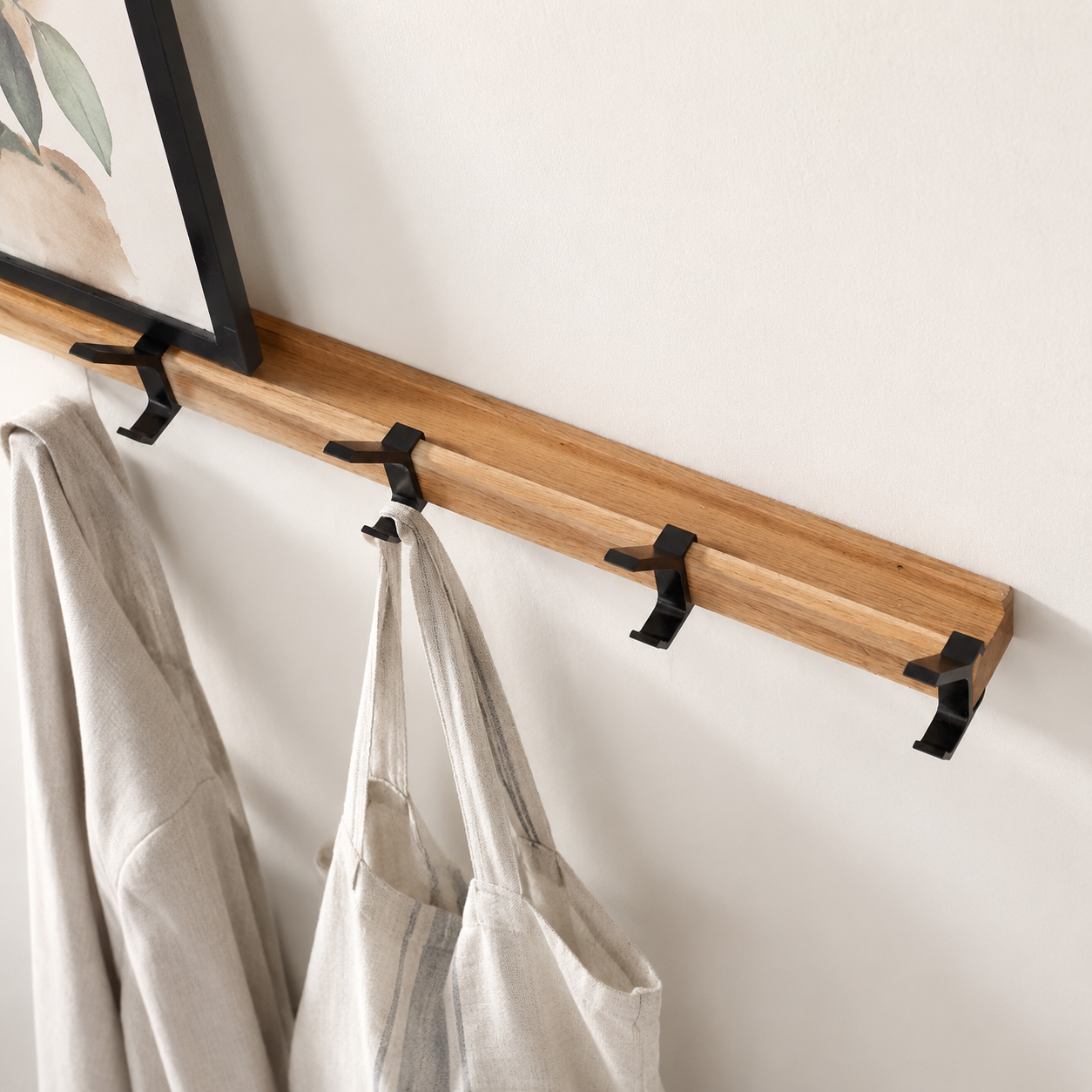 Black double-hook coat rack with wood rail holding light linen garments.