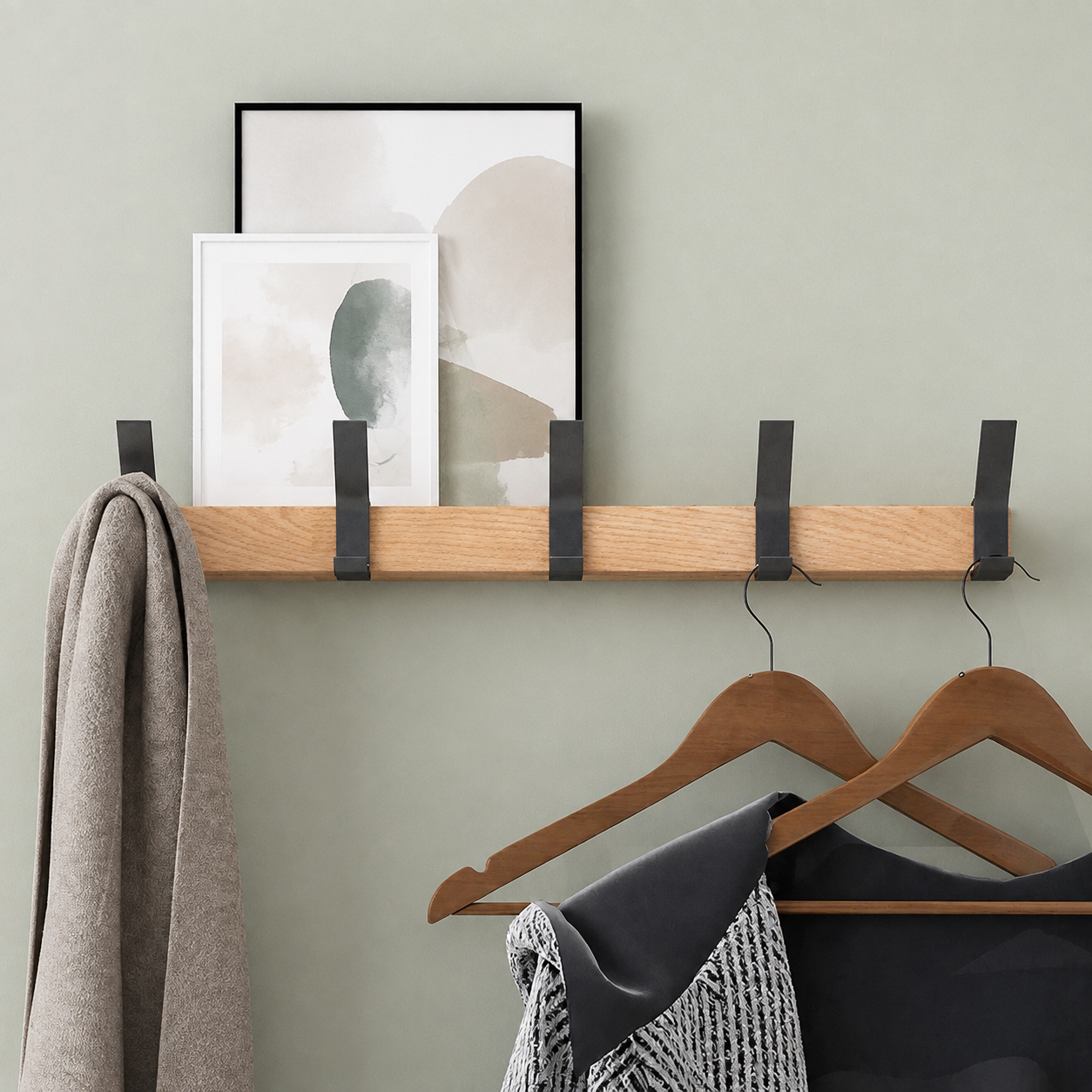 Natural wood coat rack with five black hooks, hangers and framed art.