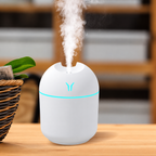 White humidifier with aqua lighting releasing mist on a wooden tabletop beside a plant
