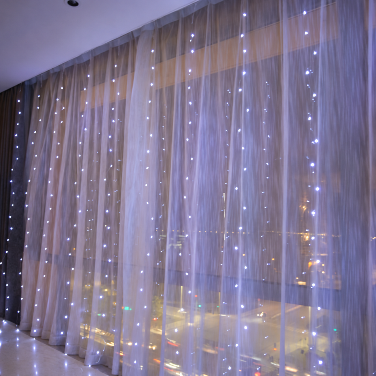 White curtain fairy lights glowing across sheer window curtains.