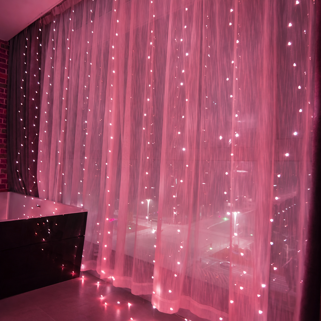 Pink curtain fairy lights glowing across sheer window curtains.