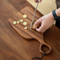 Walnut cutting board with a round handle being used to slice ginger.