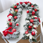 Red decorated Christmas garland with baubles and gift accents arranged on a white table