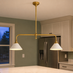 Brass two head pendant light hanging above a kitchen island with white shades illuminated.