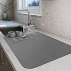 Dish drying mat in gray covering a kitchen counter beside a sink and tableware