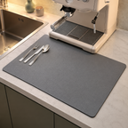 Dish drying mat in gray beneath flatware beside an espresso machine