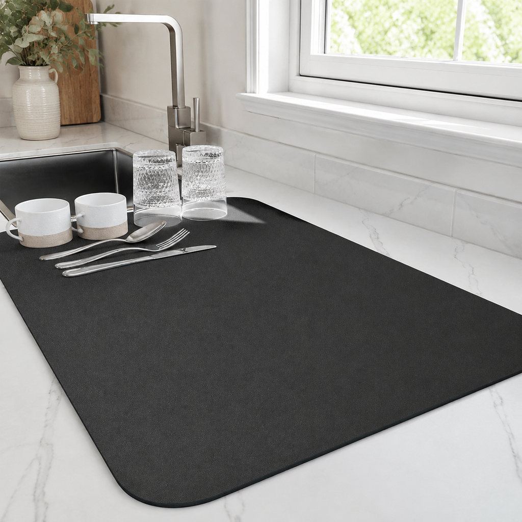 Dish drying mat in black holding cups and glasses beside a kitchen sink