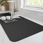 Dish drying mat in black holding cups and glasses beside a kitchen sink