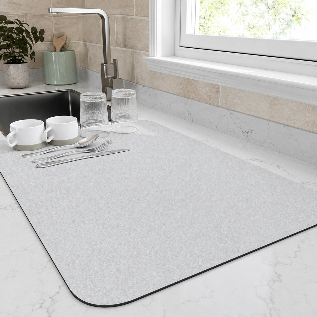 Dish drying mat in white holding cups and glasses beside a bright kitchen window